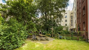Un patio con zona de barbacoa, bicicletas y un edificio de ladrillo al fondo.