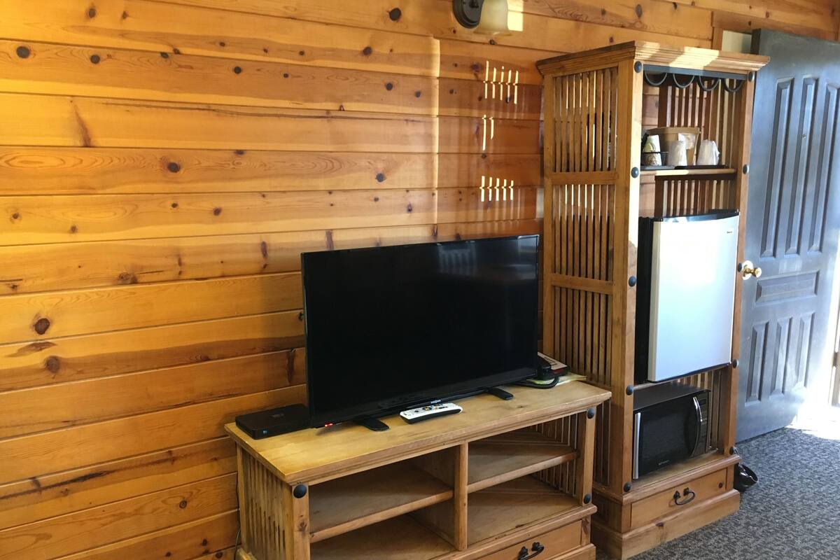 A wooden entertainment unit with a flat-screen TV, a small refrigerator, and a cabinet with shelves.