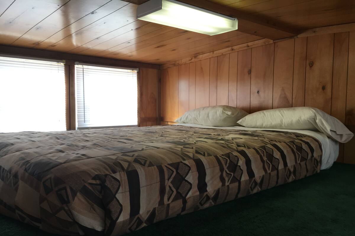 A wooden-paneled bedroom with a bed, a window with blinds, and a skylight.