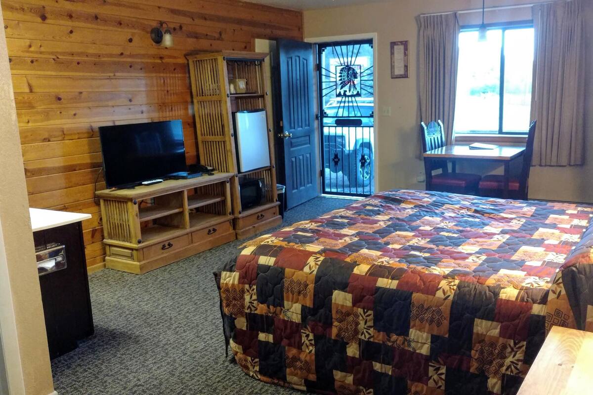 A cozy room with a large bed, a TV, a wooden wardrobe, and a desk with a chair.