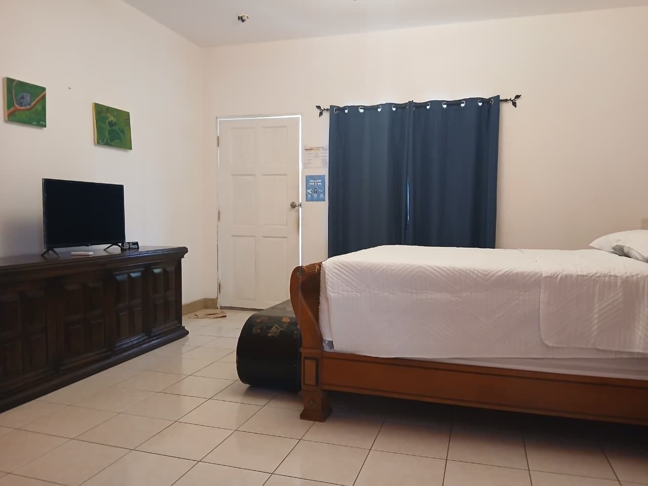 Un dormitorio con una cama, un televisor sobre un aparador y una puerta.