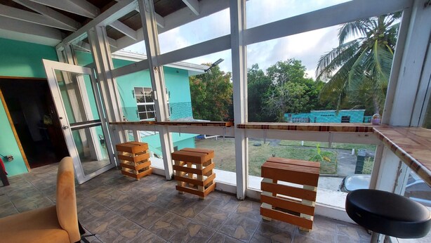 Una habitación con un ventanal grande, taburetes de madera, un banco y vistas al exterior con vegetación.