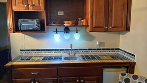 Una cocina con salpicadero de azulejos, armarios de madera, un tostador empotrado y una lámpara colgante sobre el lavamanos.