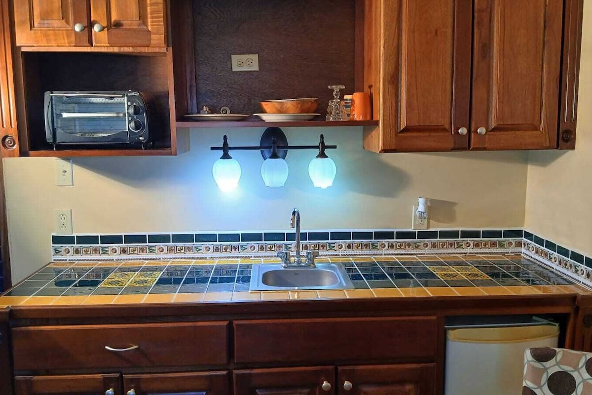 Une cuisine avec un dosseret carrelé, des armoires en bois, un grille-pain encastré et un luminaire suspendu au-dessus de l’évier.