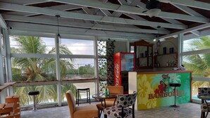 Una habitación amplia con un gran ventanal, un refrigerador Coca-Cola y una zona de bar con un letrero 'Bamboleo'.