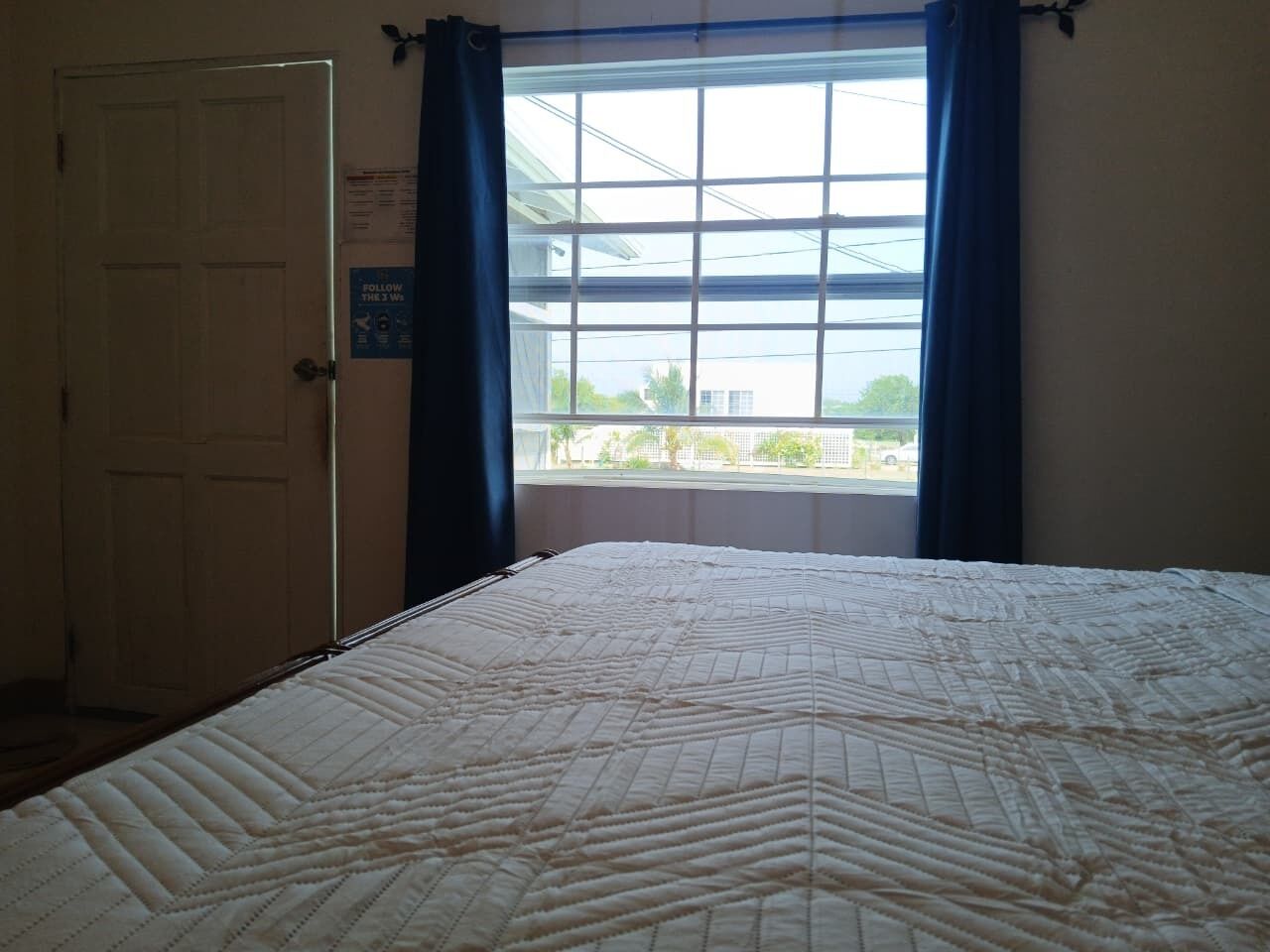 Une chambre avec un grand lit, une fenêtre avec des rideaux et une porte.