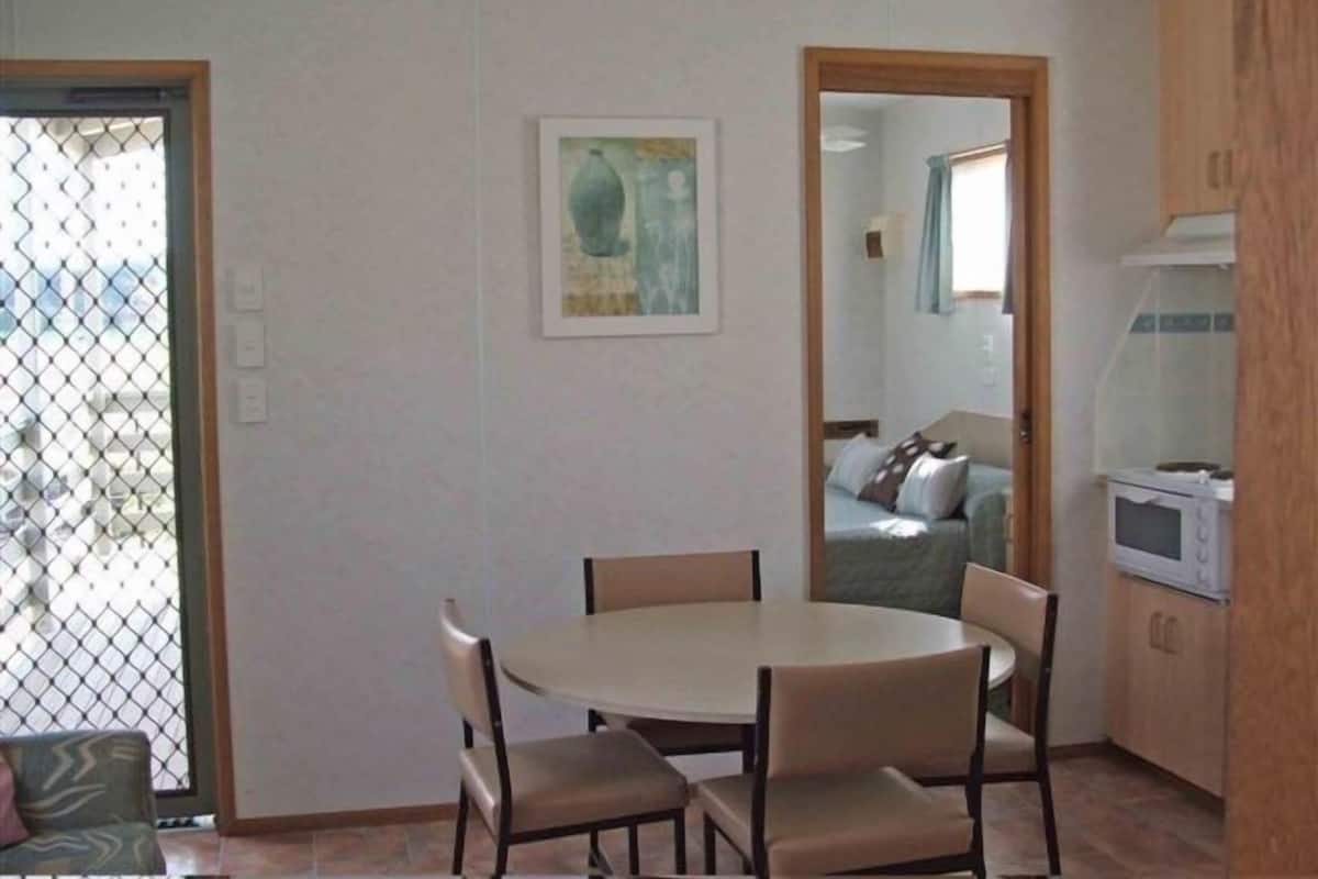 A compact living space with a dining area, kitchenette, and a view through a window with a metal screen.