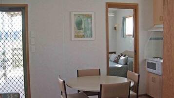 A compact living space with a dining area, kitchenette, and a view through a window with a metal screen.