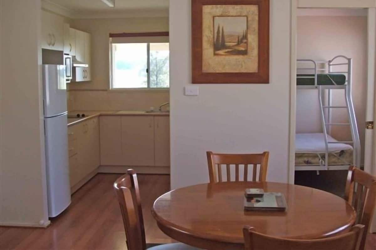A compact kitchen with a refrigerator, microwave, and sink. There's a dining table with chairs and a bunk bed with a ladder.