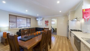A modern kitchen with wooden flooring, a dining area with a wooden table and chairs, and a visible fire blanket on the wall.