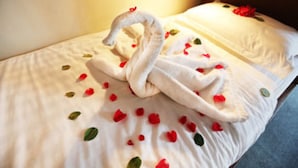 Un lit agrémenté d’une serviette en forme de cygne et de pétales de rose éparpillés.