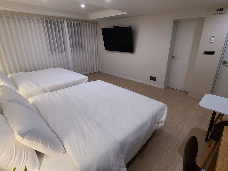 Ein Hotelzimmer mit zwei Betten, einem an der Wand montierten Fernseher, einem Schreibtisch mit Pflanze und einer Tür mit der Beschriftung '603 HOTEL Andrest'.