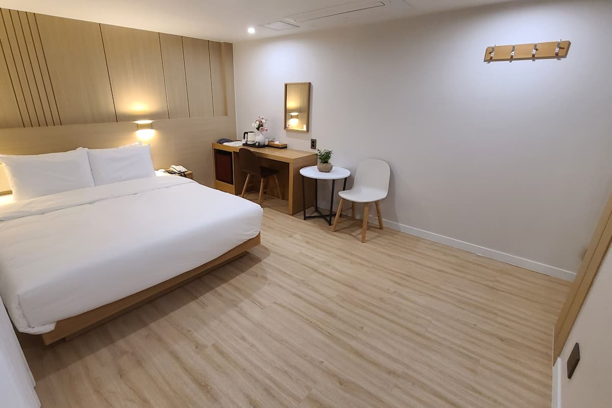 A modern hotel room with a large bed, a desk, a chair, and a small table with a plant.