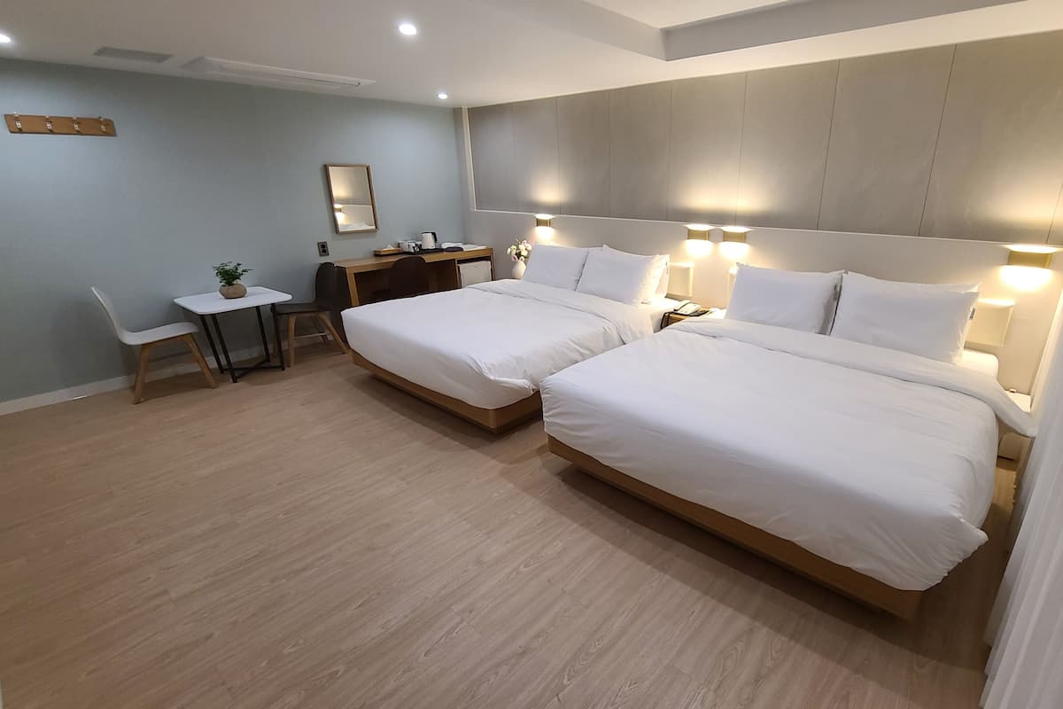 A hotel room with two single beds, a desk with a chair, a small table, and a mirror on the wall.