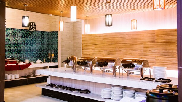 A modern hotel breakfast area with a wooden ceiling, a tiled backsplash, and a buffet setup.