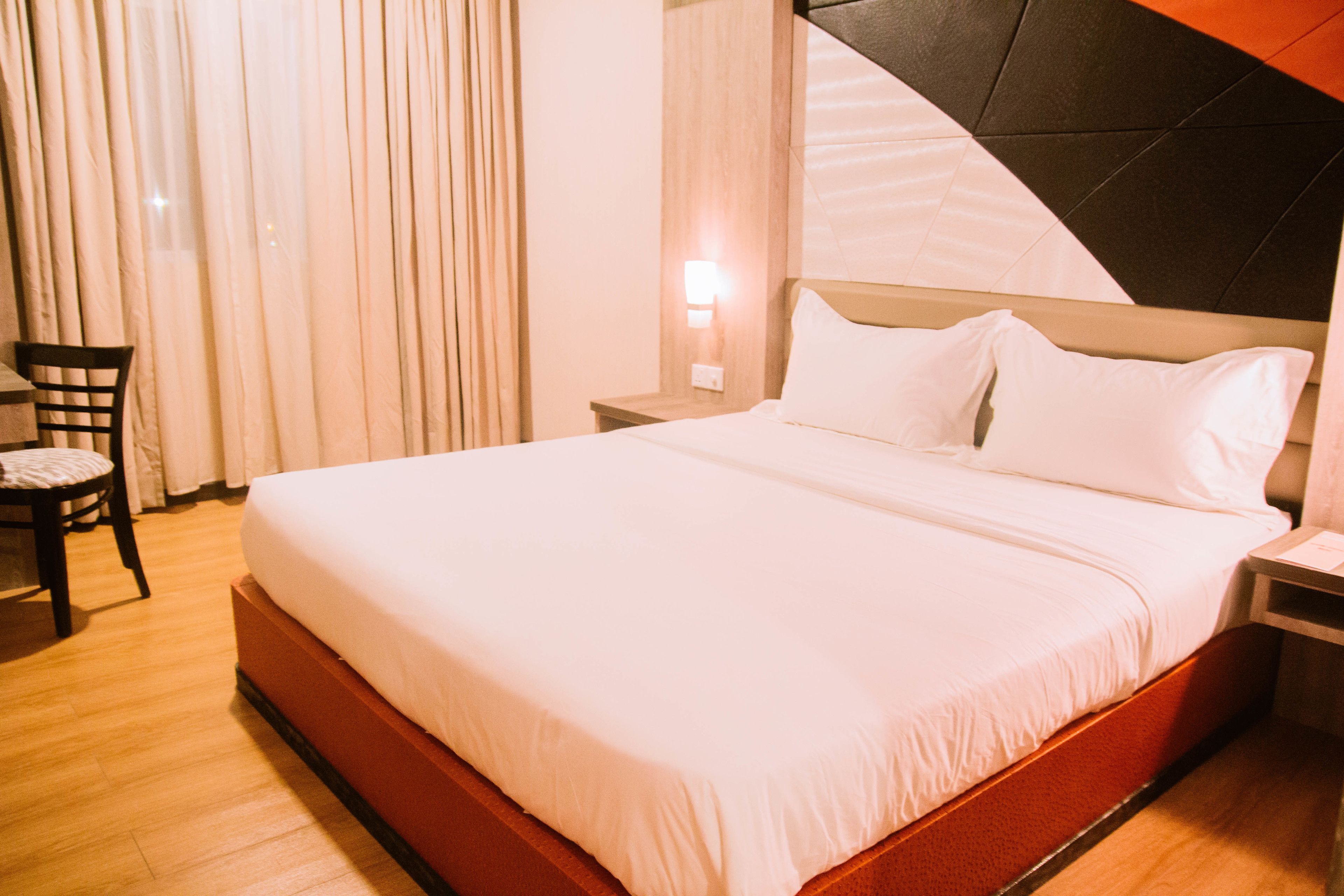A hotel room with a large bed, a nightstand, a chair, and a wall-mounted lamp.