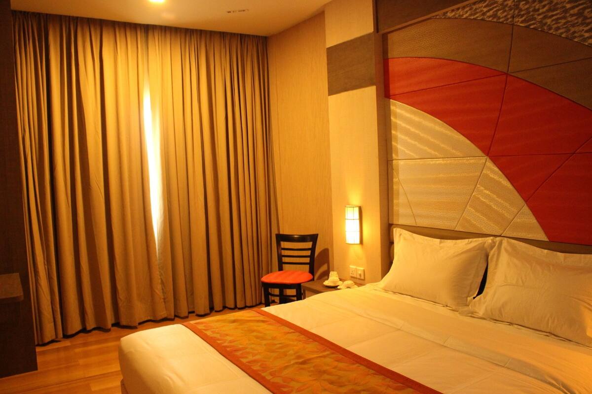 A hotel room with a bed, curtains, a chair, and a wall-mounted light.