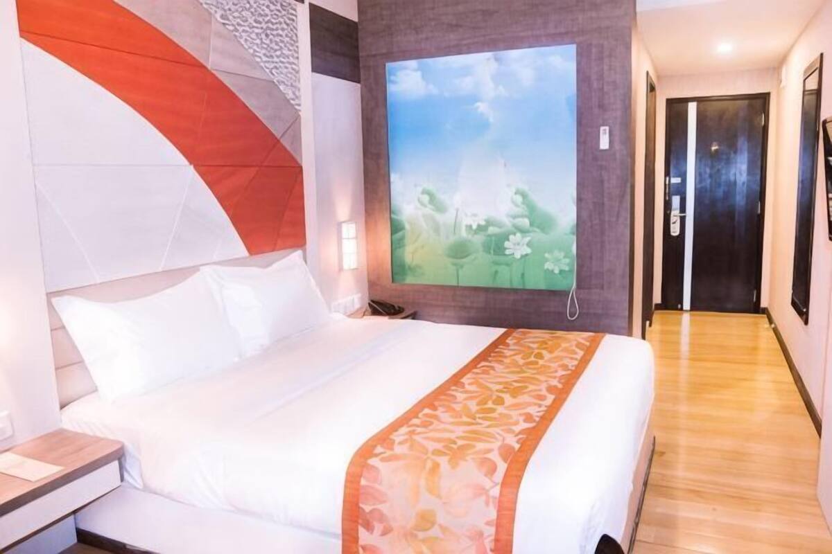 A hotel room with a large bed, a painting of a landscape, and a wooden floor.
