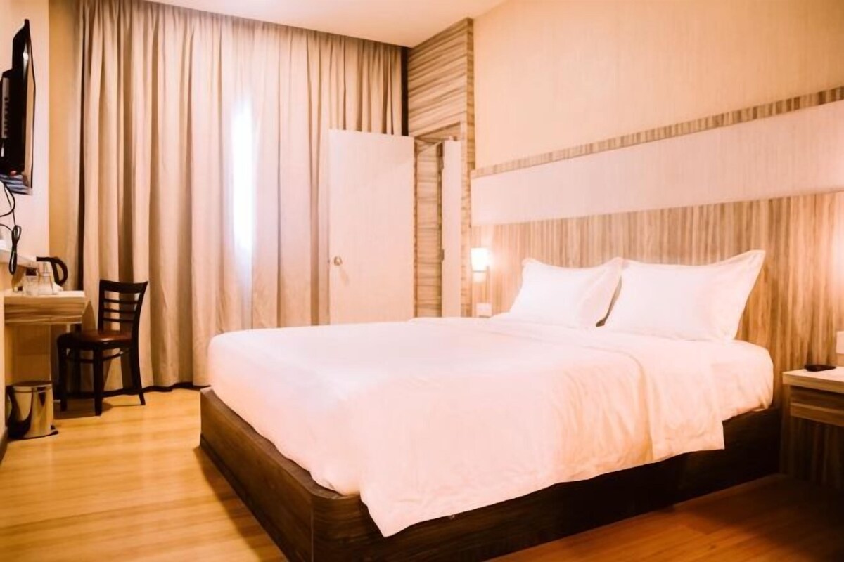 Une chambre d’hôtel avec un grand lit, un bureau avec une chaise, une télévision et une fenêtre avec des rideaux.