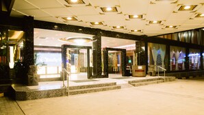 A hotel lobby with marble flooring, a reception area with a glass door, and a large statue.