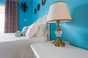 Une chambre à coucher avec un lit blanc, une table de chevet blanche, une lampe en laiton et un mur bleu.