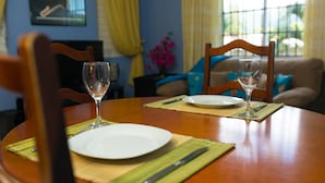 Una mesa de comedor dispuesta con platos, cubiertos y copas de vino, con un sofá y cojines decorativos al fondo.
