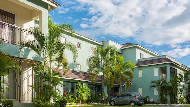Un edificio residencial con fachada verde, varias ventanas y un coche estacionado al frente.