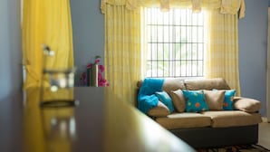 Una sala de estar con sofá, cortinas amarillas y una ventana con rejas.