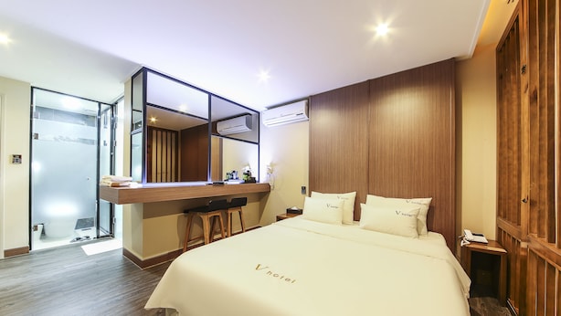 A hotel room with a large bed, a wooden headboard, a built-in desk with stools, a mirror, and a shower area. - Number25 Hotel (Busan)