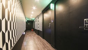 A hallway with patterned walls and a tiled floor, leading to a door with a lock and a light switch. - Number25 Hotel (Busan)