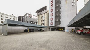 A parking area with multiple cars, a covered waiting area, and a building with a prominent sign. - Number25 Hotel (Busan)