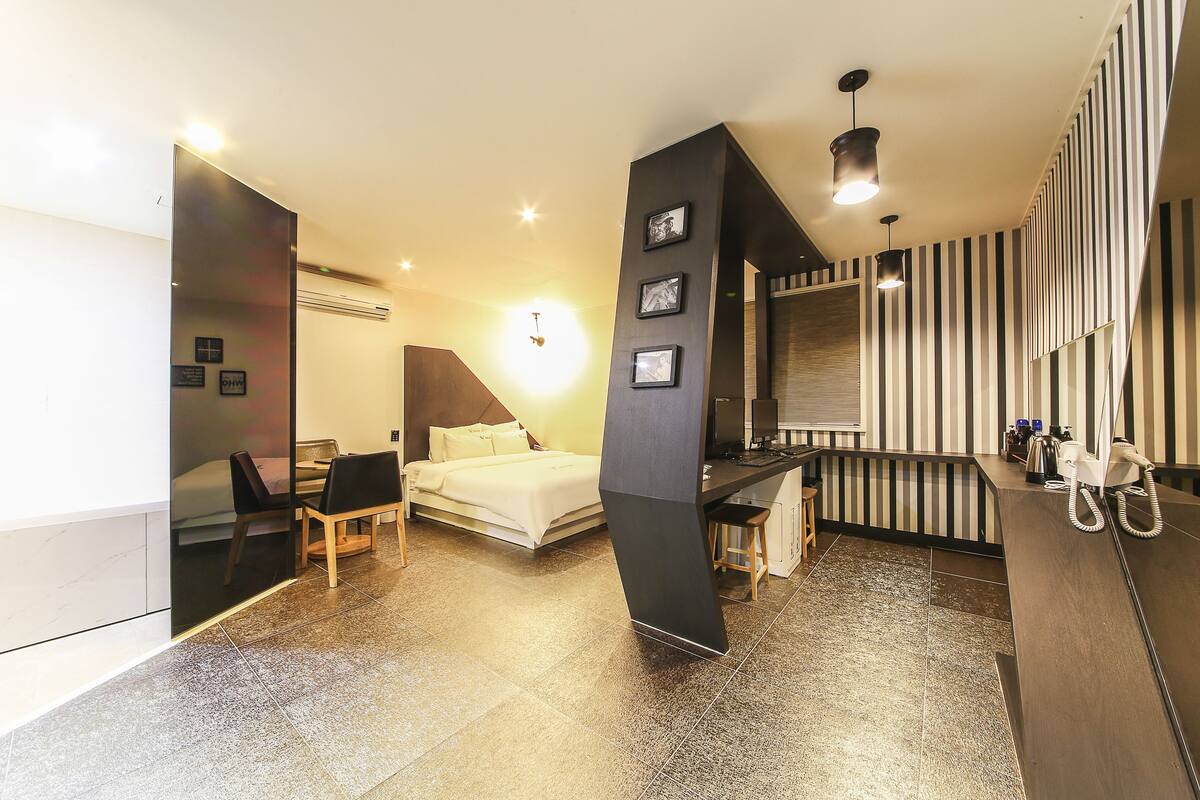 A modern hotel room with a bed, desk, and chair, a bathroom with a shower, and striped walls.