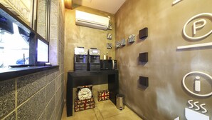 A hotel reception area with a counter, coffee machines, a trash bin, and a wall with a 'P' and 'i' logo. - Number25 Hotel (Busan)