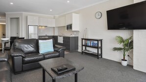 A modern living room with a leather sofa, a coffee table, and a flat-screen TV mounted on the wall. - Crown Apartments (Merimbula)