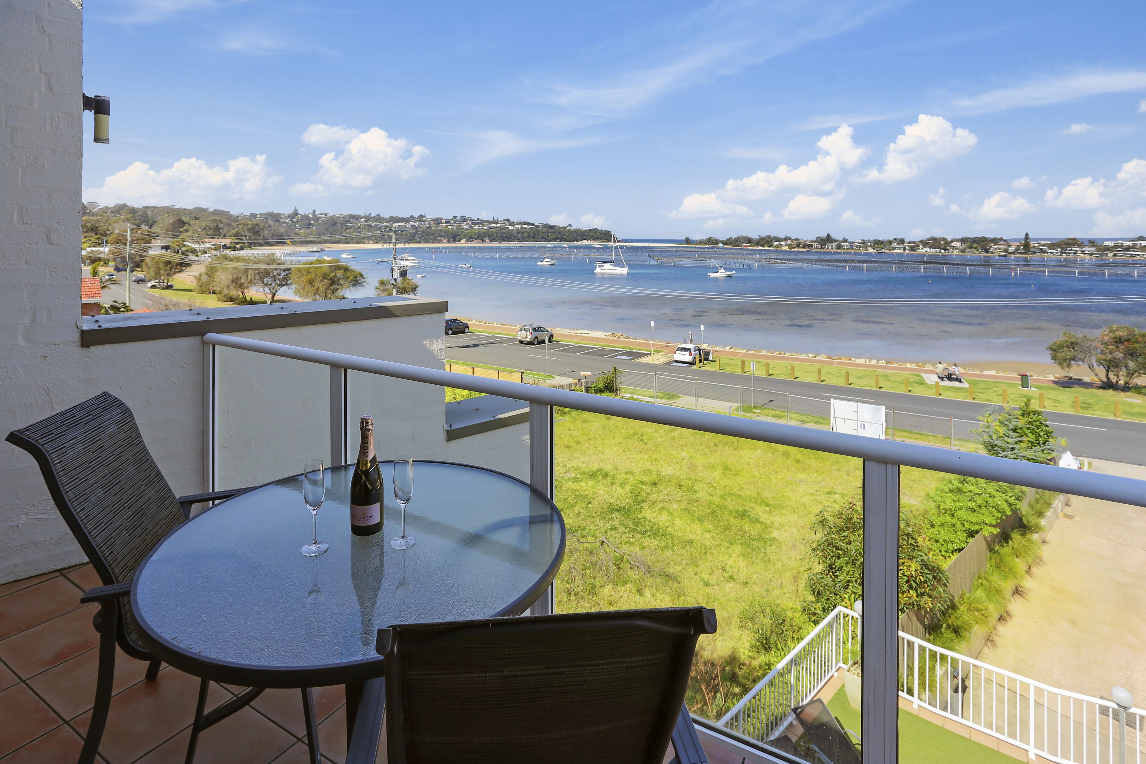 Un balcon avec une table et des chaises donnant sur une marina, où l’on peut admirer des bateaux et une plage.