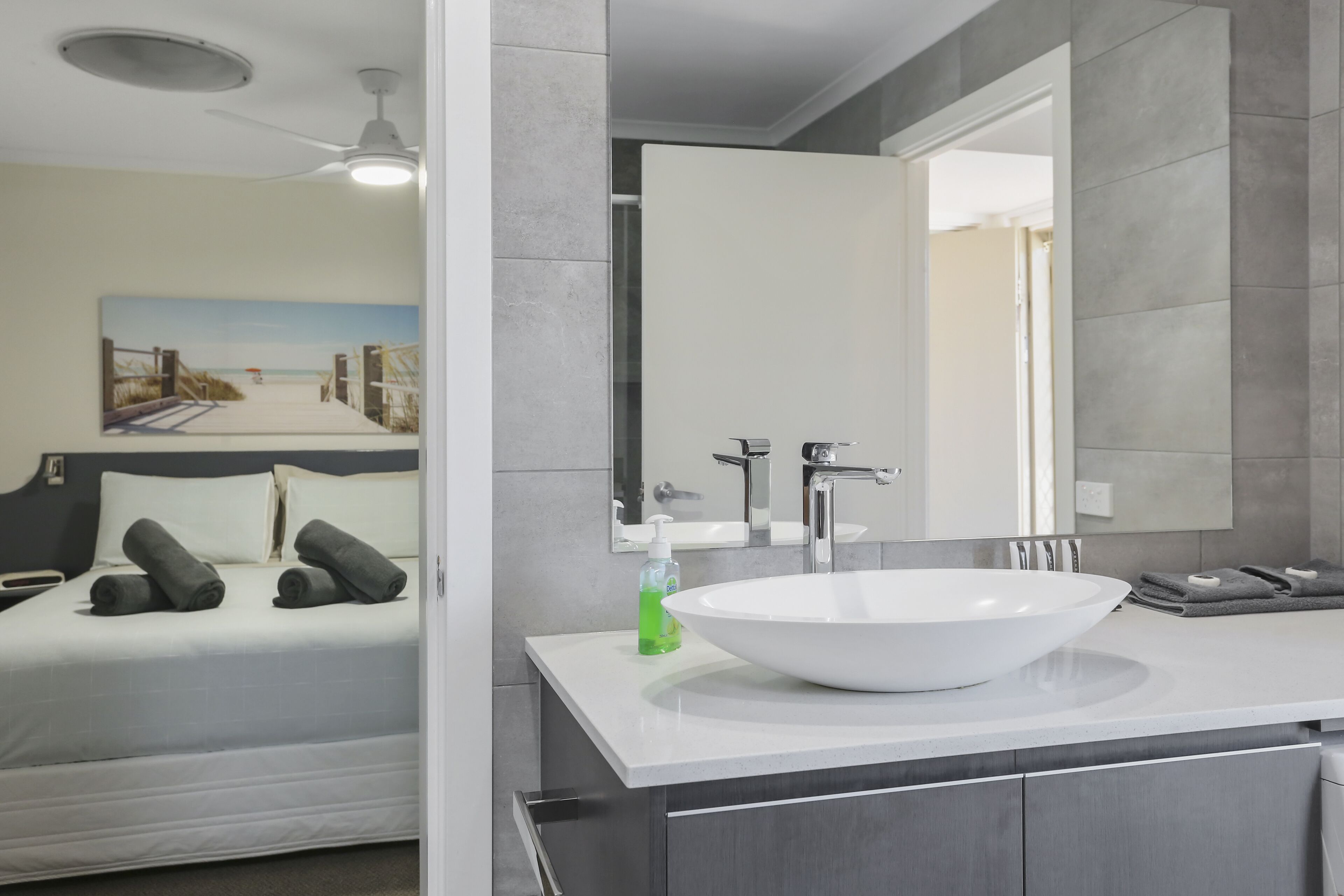 Ein modernes Badezimmer mit einem großen, weißen Waschbecken, einem Spiegel und einem Deckenventilator.