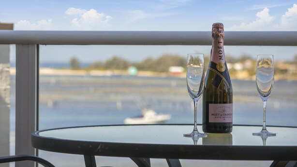 A bottle of Moet & Chandon champagne on a table with two glasses, overlooking a body of water. - Crown Apartments (Merimbula)