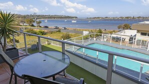 A balcony with a view of a swimming pool and a marina. - Crown Apartments (Merimbula)