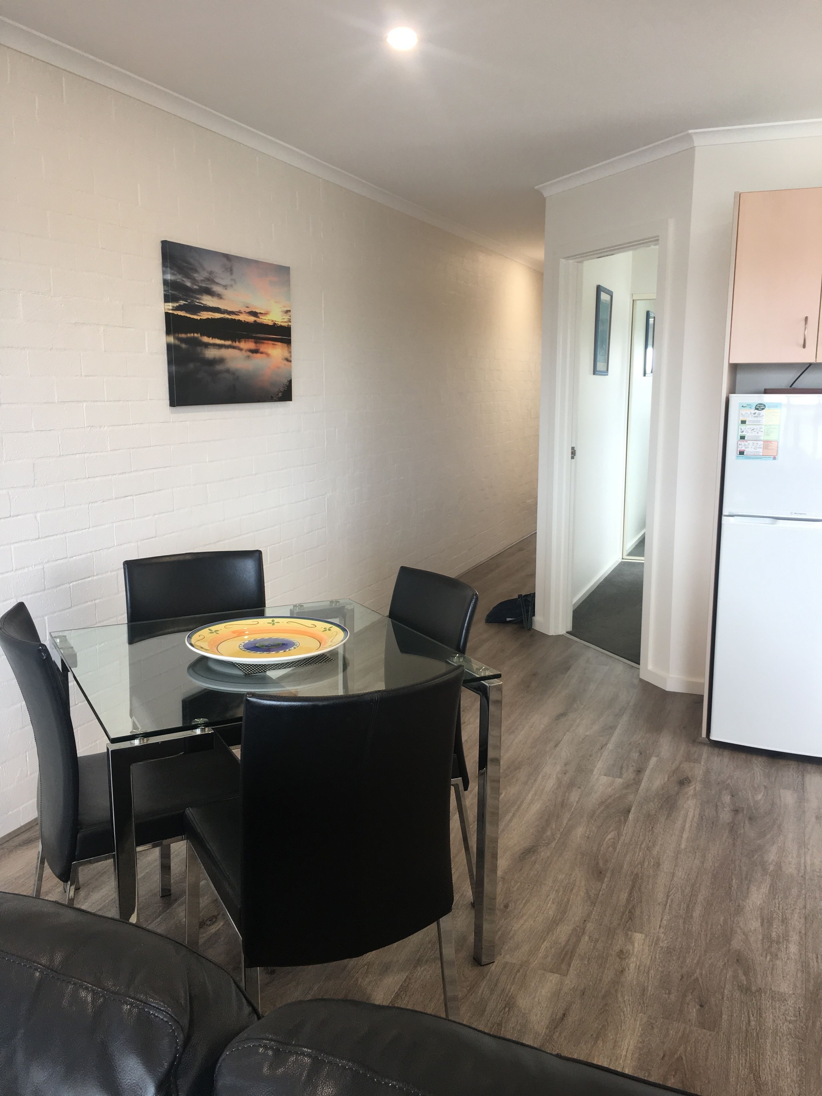 Una cocina moderna con refrigerador, una mesa de comedor con sillas y un cuadro en la pared.