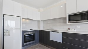 A modern kitchen with white and dark cabinetry, a built-in oven, a dishwasher, and a microwave. - Crown Apartments (Merimbula)