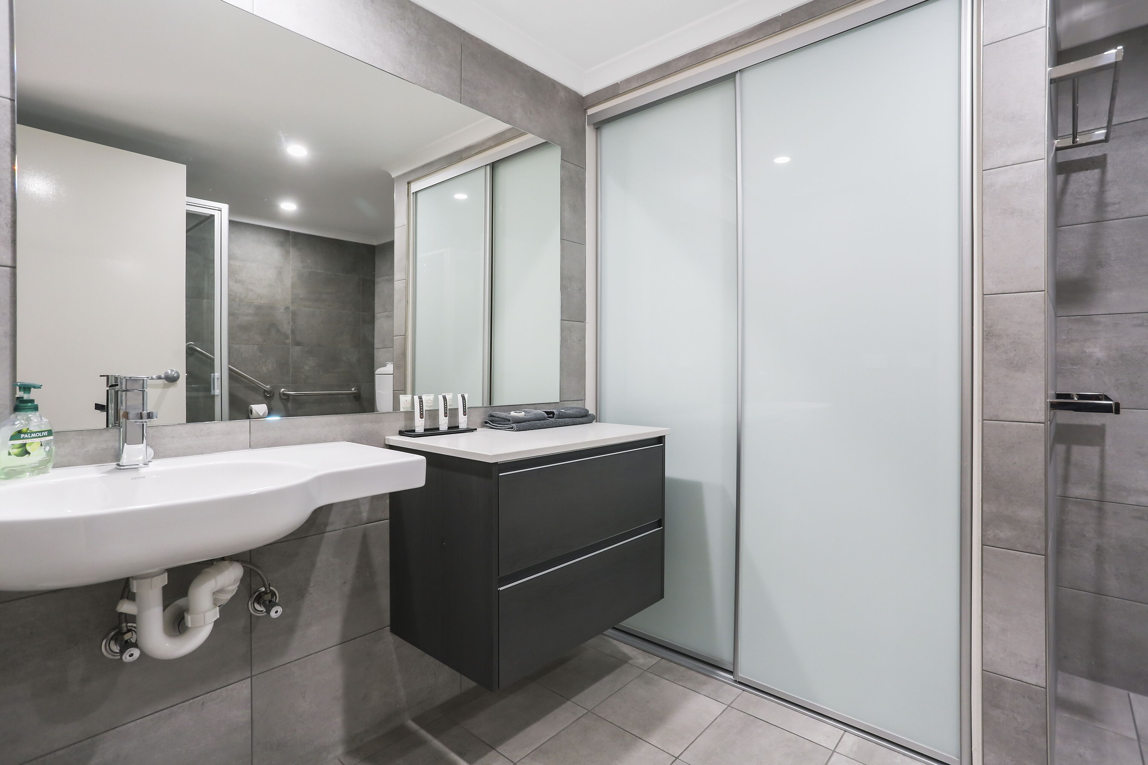 Een moderne badkamer met een witte wasbak, een zwart kastje en een douchecabine van glas.