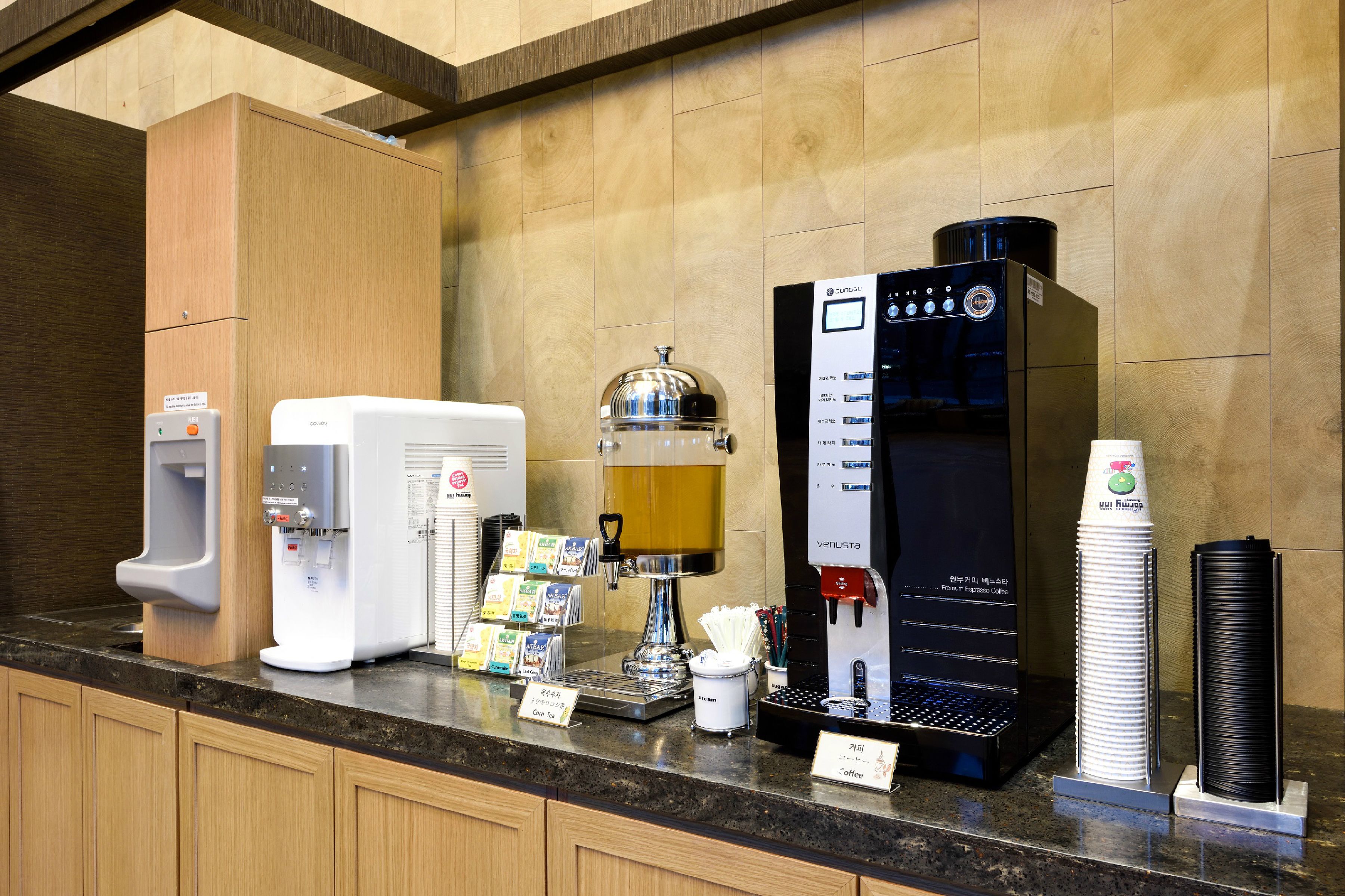 Una estación de café con varias máquinas de café, un dispensador de agua y una pila de vasos desechables.