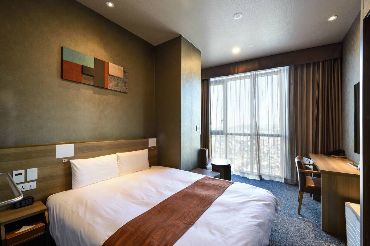 A hotel room with a large bed, a desk, a chair, and a TV.