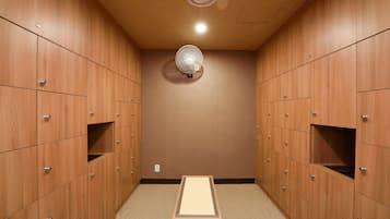 A locker room with wooden lockers, a standing fan, and a small table.