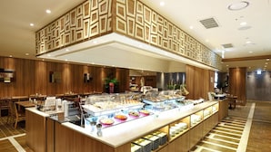 Zona de buffet amb diverses estacions de menjar, panells de fusta i un dibuix de sostre a escacs.