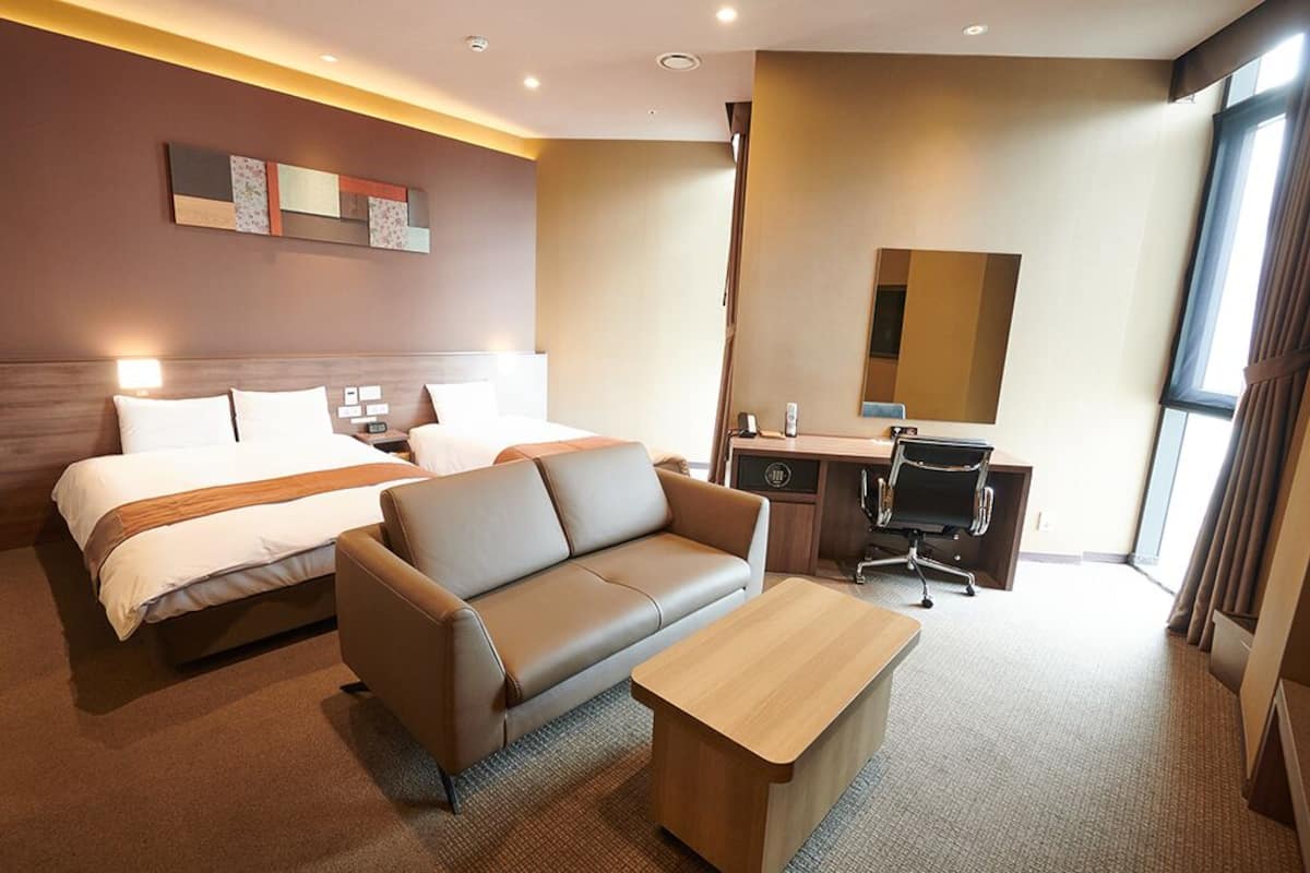 A hotel room with a bed, a sofa, a desk, and a mirror.
