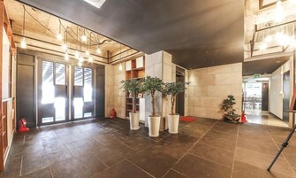 A spacious lobby with a modern design, featuring a large entrance with glass doors, potted plants, and a tiled floor.