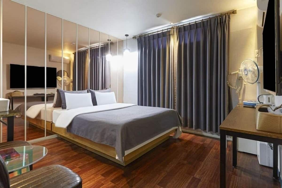 A modern hotel room with a large bed, a desk, a chair, a TV, and a mirror.