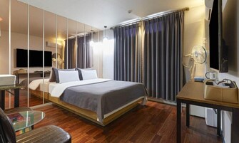 Una habitación de hotel moderna con una cama grande, un escritorio, una silla, un televisor y un espejo.