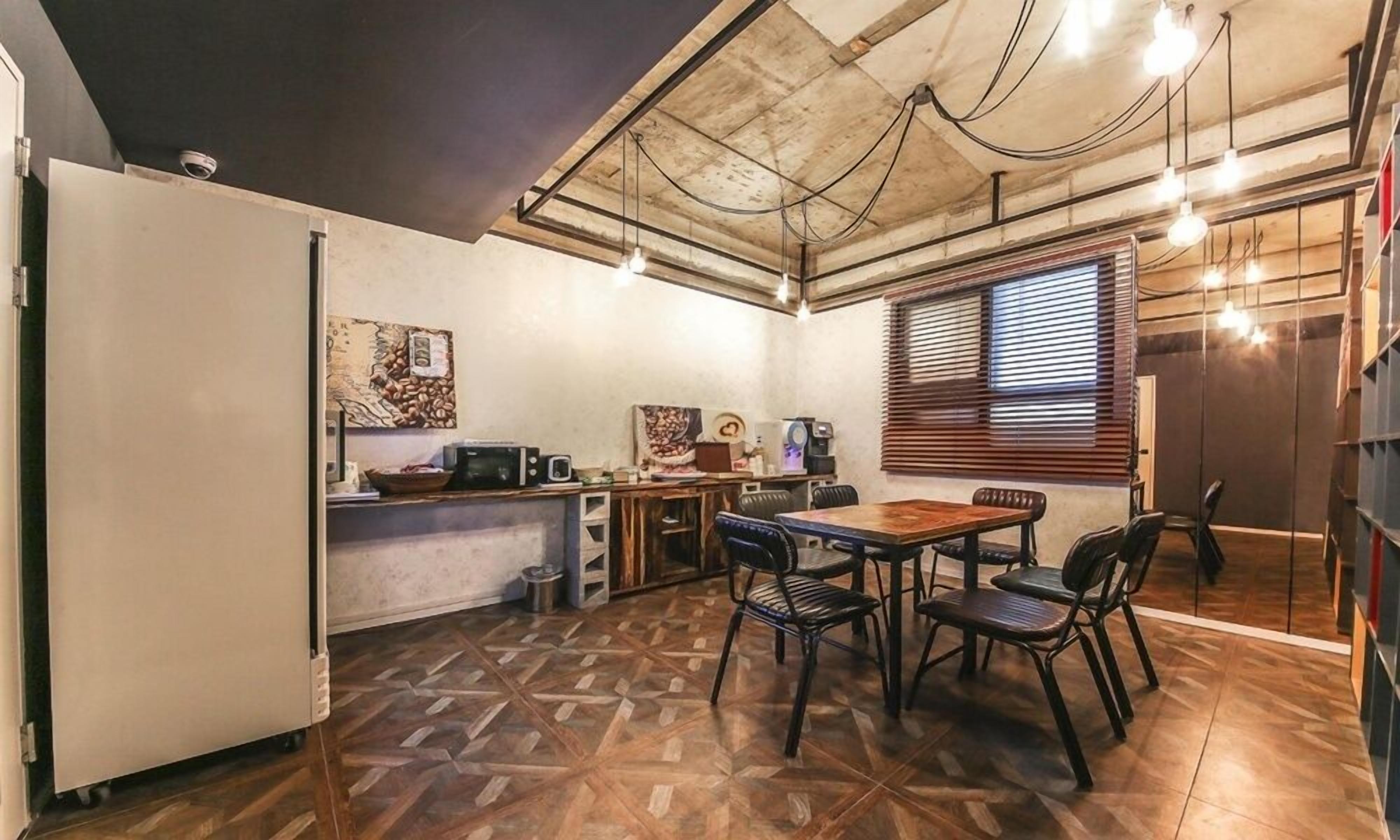 A compact kitchen with a dining area, featuring a wooden table and chairs, a coffee machine, and a microwave.